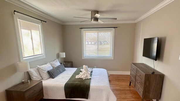 Une chambre à coucher comprenant un lit, des tables de chevet, une commode, un ventilateur de plafond et un téléviseur.