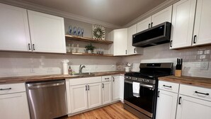 Une cuisine moderne avec des meubles blancs, un lave-vaisselle en acier inoxydable, une cuisinière noire et des plans de travail en bois.