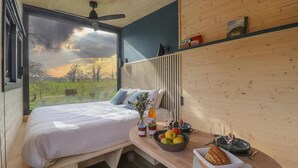 A bedroom with a bed, a bedside table with breakfast items, a window with a view of the countryside, and a ceiling fan.