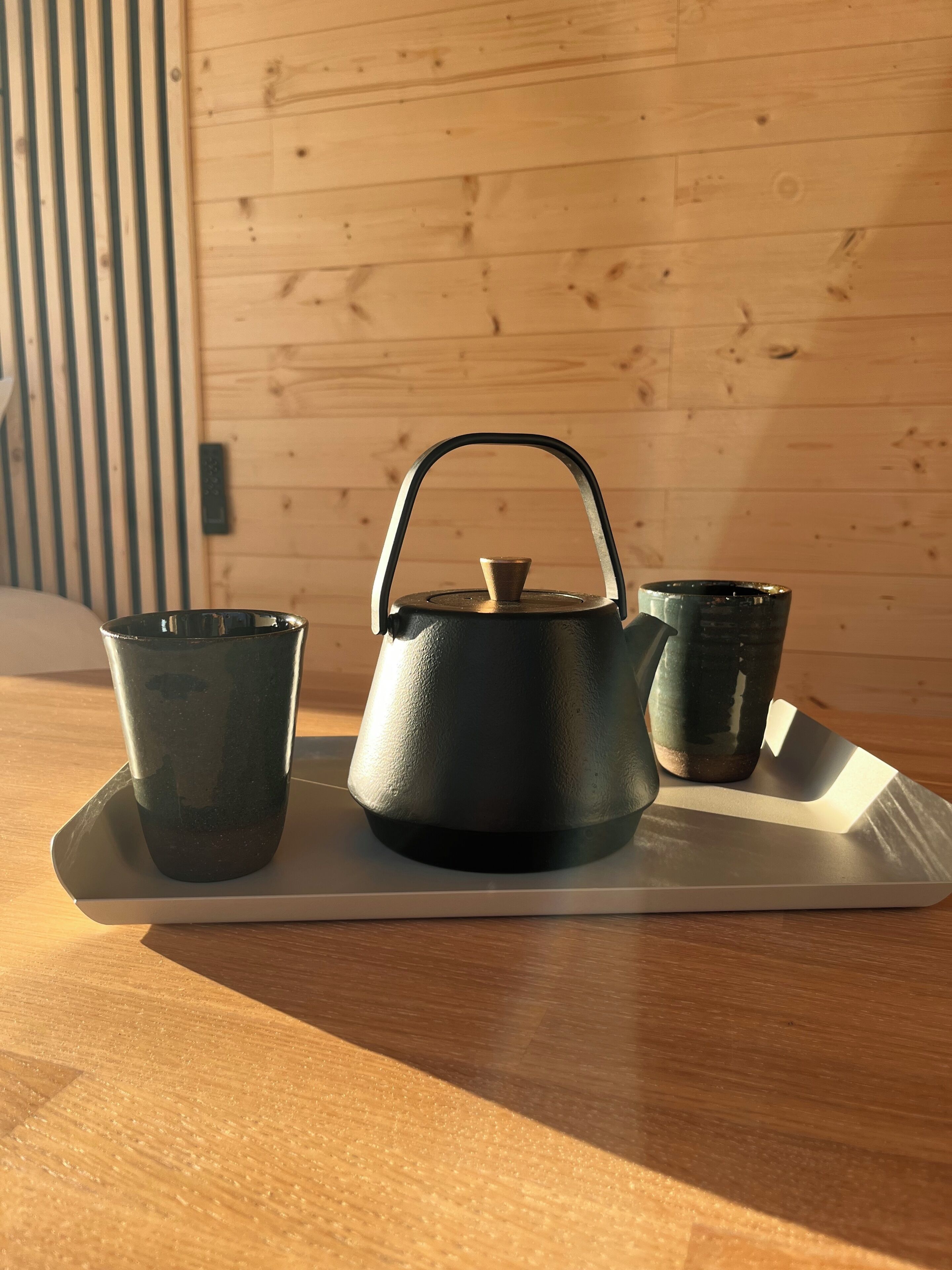 A wooden table with a tray holding a black kettle and two dark cups.