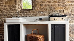 A rustic kitchen with a stone wall, a window, a sink, a stove, and a woven basket.