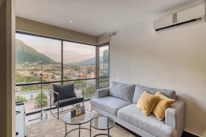 Una sala de estar moderna con un gran ventanal, un sofá gris, un sillón negro y una pequeña mesa de centro.