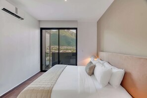 Un dormitorio con una cama, un mesita de noche, una lámpara y vistas a un paisaje montañoso a través de un ventanal.