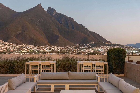 A rooftop terrace with outdoor seating, a view of a cityscape, and mountains in the background.