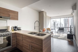A modern kitchen with a stove, sink, and coffee maker, and a living area with a sofa and a view of the city. - 2Bed/2Bath, Pool, Gym & Mountain Views! (Monterrey)