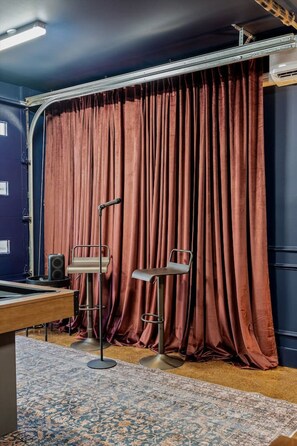 A room with a dark blue door, a red curtain, a standing desk, two chairs, a speaker, and a patterned rug. - The Polo Mansion | Classic Americana + Amenities (Nashville)