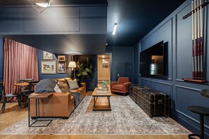 Ein modernes Wohnzimmer mit einer Couch, einem Couchtisch und einem Fernseher. Eine Pflanze, eine Lampe und ein Koffer sind ebenfalls vorhanden.