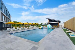 Ein Schwimmbecken mit Liegestühlen und Sonnenschirmen, eine überdachte Sitzgelegenheit und ein Holzzaun.