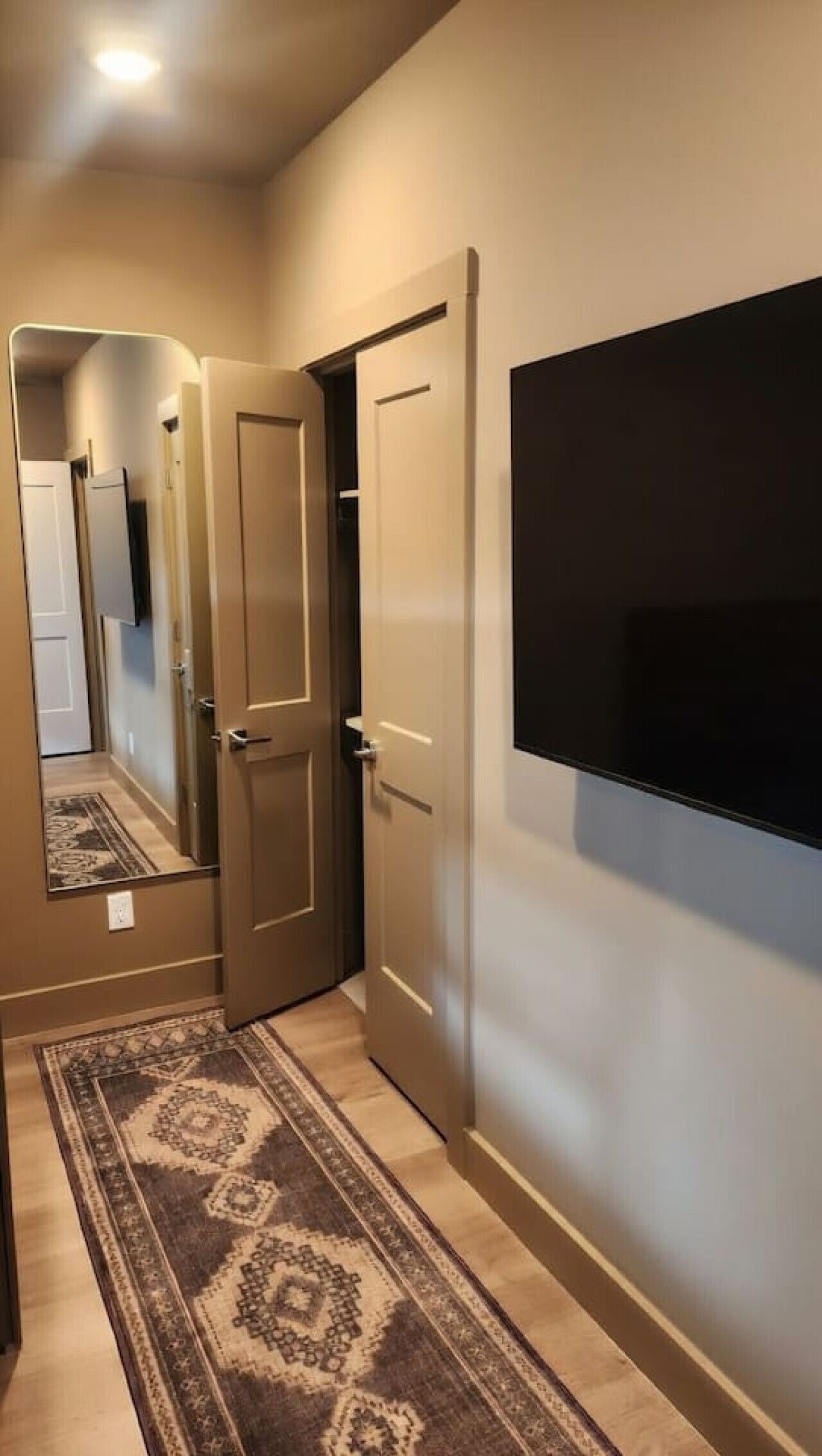 Um corredor com tapete estampado, uma televisão de tela plana na parede e uma porta que dá para outro cômodo.