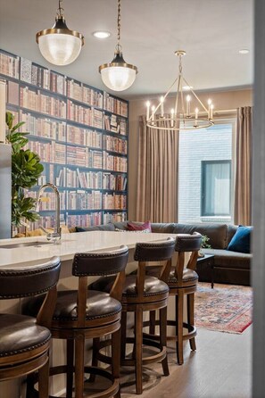 Une cuisine moderne dotée d’un îlot central, de tabourets de bar et d’une bibliothèque remplie de livres.