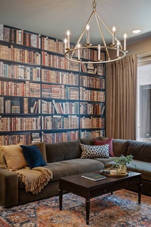 A cozy living room with a large bookshelf, a leather sofa, and a coffee table. - The Polo Mansion | Classic Americana + Amenities (Nashville)