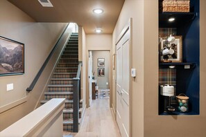 A hallway with a staircase, a door, and a shelf with items. - The Polo Mansion | Classic Americana + Amenities (Nashville)