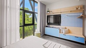 Una habitación de hotel moderna con un ventanal grande, un televisor de pantalla plana, una cama, un escritorio y un panel de corcho en la pared.