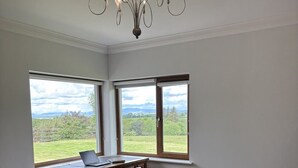Ein Schlafzimmer mit einem großen Bett, einem Schreibtisch mit einem Laptop und zwei Fenstern mit Blick auf eine grüne Landschaft.
