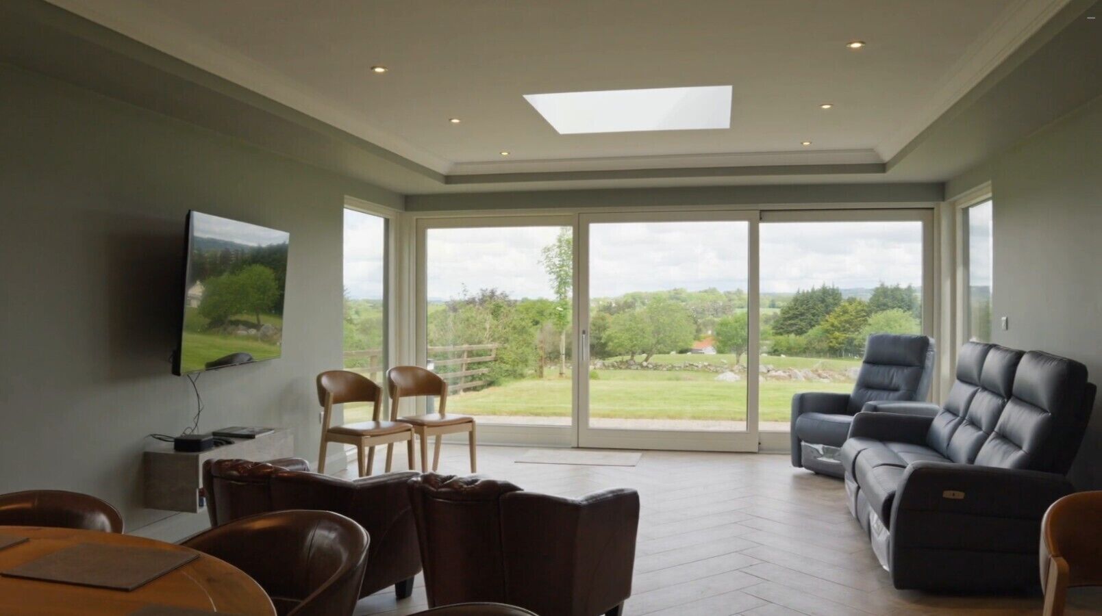 Un vaste salon doté d’une grande porte-fenêtre coulissante donnant sur un balcon, d’un téléviseur à écran plat fixé au mur et d’un coin salon confortable avec des canapés et des fauteuils en cuir.