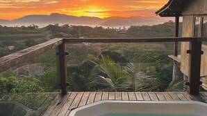Ein Whirlpool auf einer Holzterrasse mit Blick auf einen Sonnenuntergang über Bergen und Grünflächen.