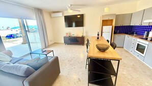 Ein modernes Wohnzimmer mit Sofa, Esstisch und Küchenbereich, inklusive Fernseher und Schränken.