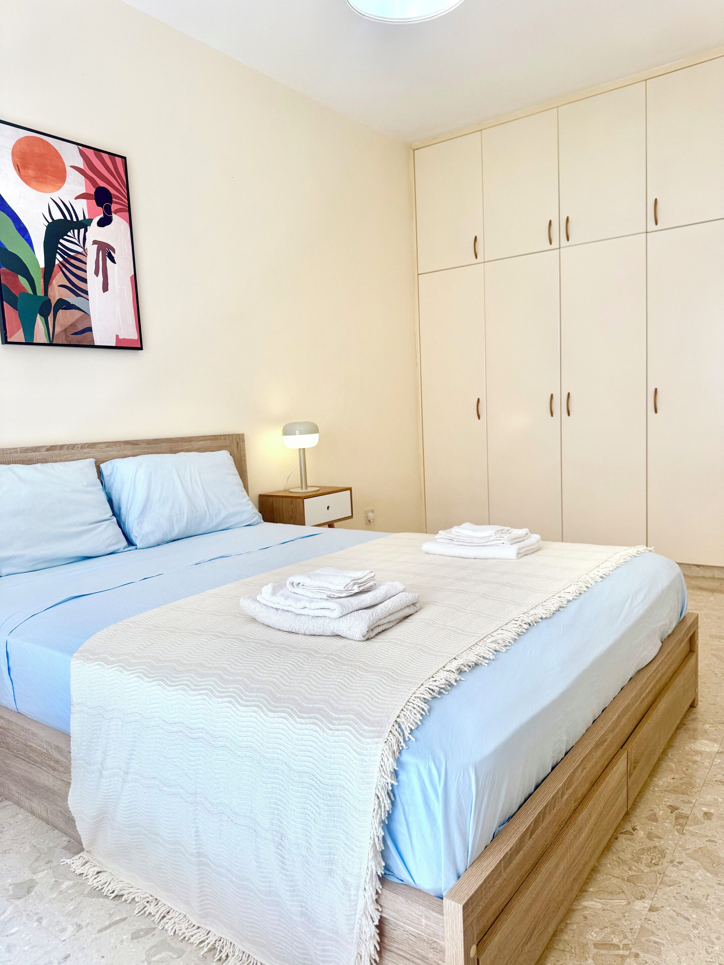 A bedroom with a bed, a nightstand, a lamp, and a wardrobe.
