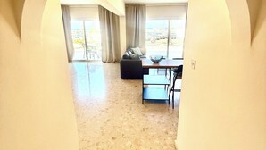 Ein geräumiger Raum mit hoher Decke, großem Fenster, einer Couch und einem Esstisch.