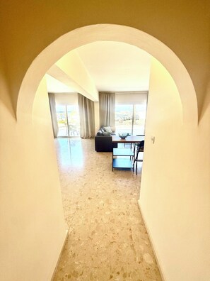A spacious room with a high ceiling, a large window, a sofa, and a dining table. - Stunning Harbour-View Apartment with Pool & Generous Terrace in Latchi (Poli Chrysochous)