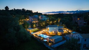 Una zona residencial con varias casas, una piscina y un camino de entrada bien iluminado al anochecer.