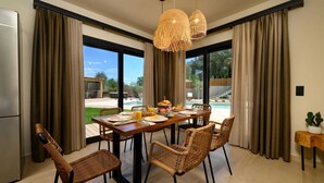 Un comedor con una mesa dispuesta para el desayuno, sillas de mimbre y vistas a una piscina.