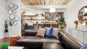 Un soggiorno moderno con un divano in pelle, un soffitto in legno e una cucina sullo sfondo.
