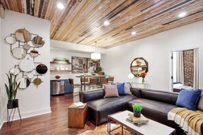A modern living room with a sectional sofa, a coffee table, and a dining area in the background. - 6BR Savannah Condo Combo | Walk to Nightlife (Savannah)