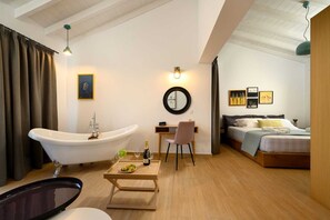 A room with a bathtub, a desk with a chair, a bed, and artwork on the walls.