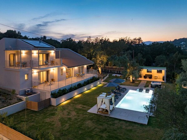 A two-story modern house with a swimming pool, outdoor seating, and a well-lit patio area.
