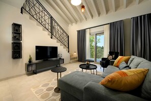 Ein modernes Wohnzimmer mit Treppe, Flachbildfernseher, Sofa und einem Balkon mit Vorhängen.