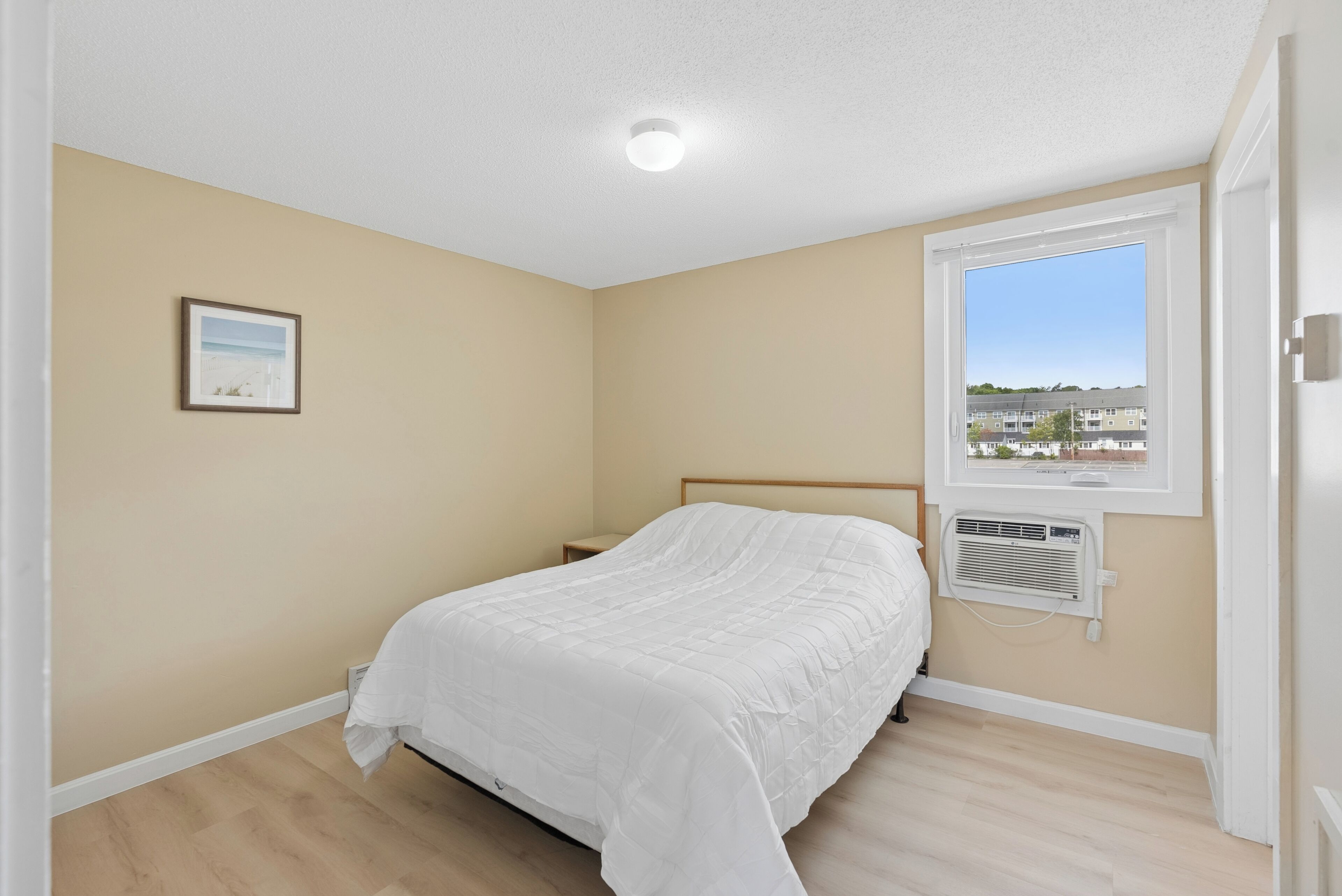 A bedroom with a bed, a window with a view, a picture on the wall, and a ceiling light.