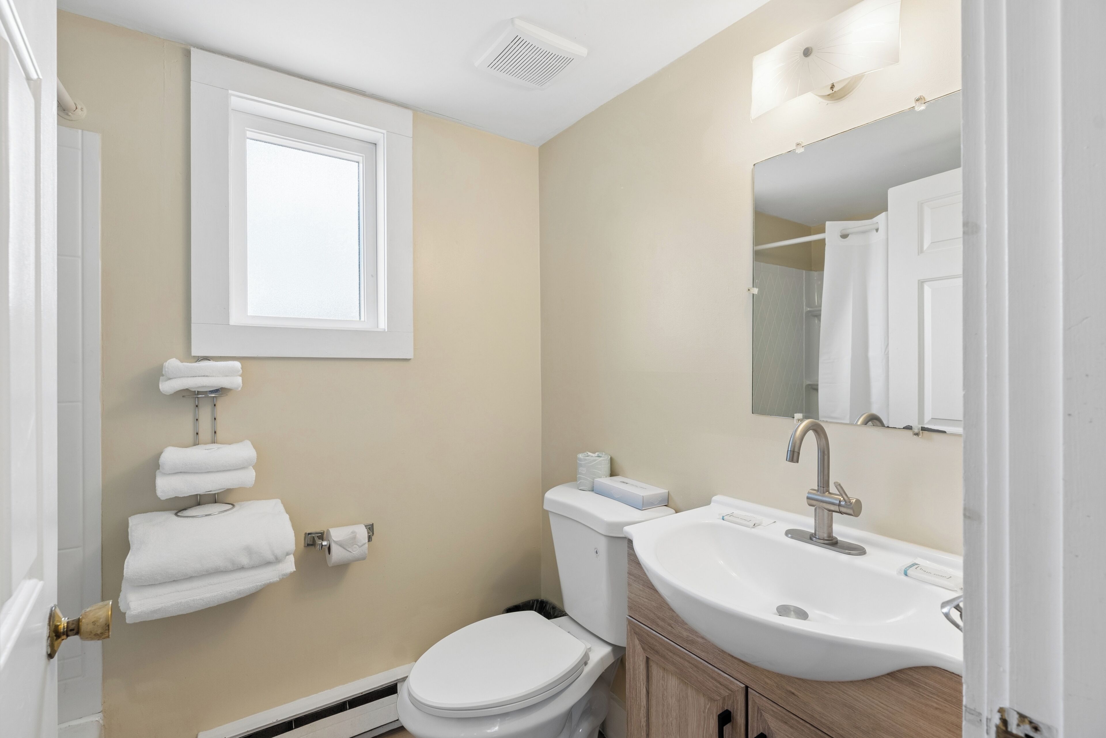 Un baño con inodoro, lavamanos, toallero y ventana.