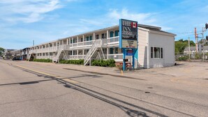 A motel with a blue sign, a staircase leading to the entrance, and a parking sign indicating customer parking only. - The Inn at SOHO Square (Old Orchard Beach)