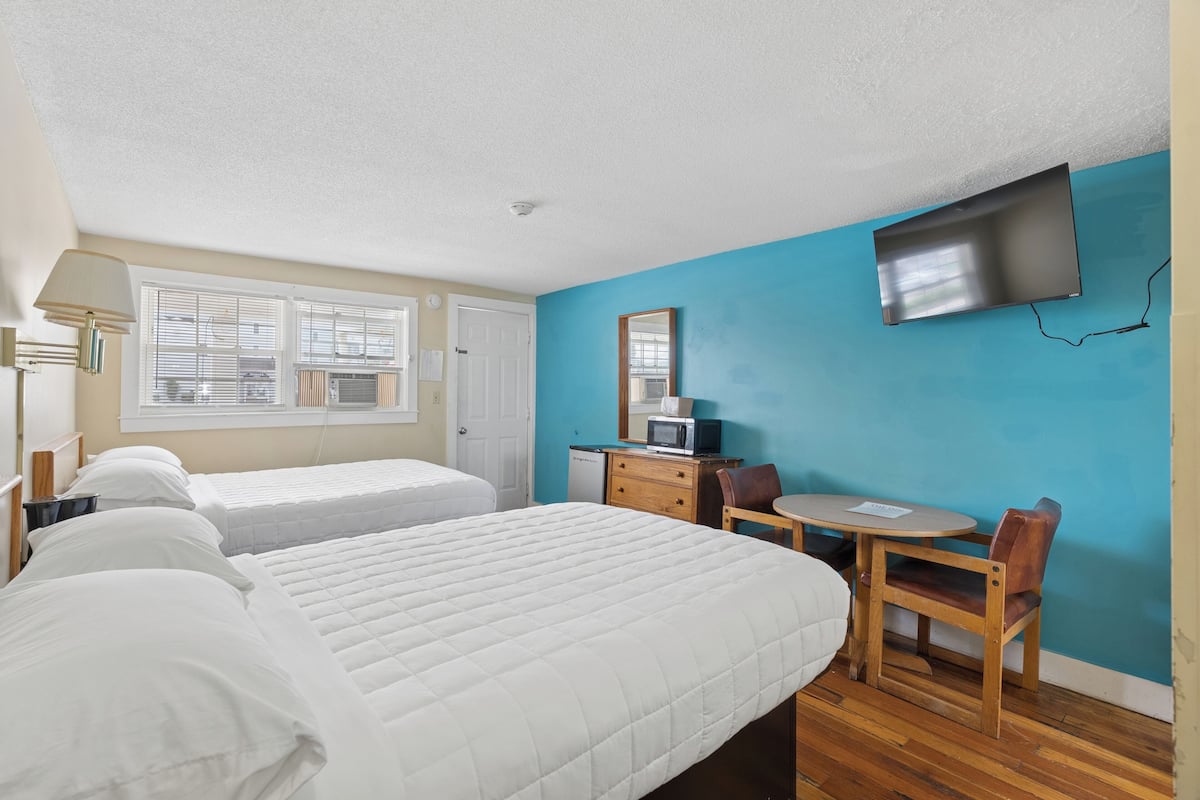 Une chambre avec deux lits, un bureau, une chaise, une télévision et une fenêtre avec des stores.