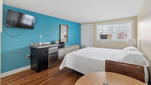 A hotel room with a bed, a desk, a kitchenette, a TV, and a window with blinds. - The Inn at SOHO Square (Old Orchard Beach)