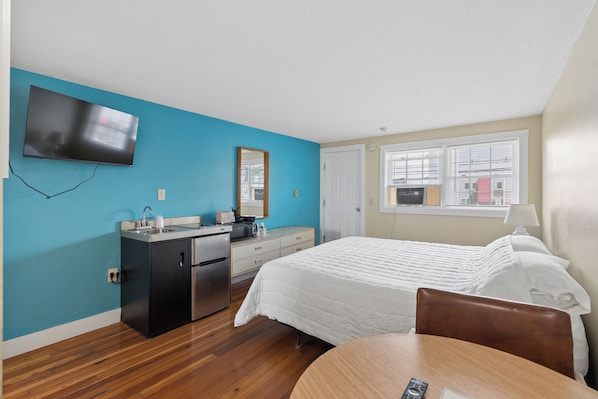 Une chambre dâhĂŽtel Ă©quipĂ©e dâun lit, dâun bureau, dâune kitchenette, dâune tĂ©lĂ©vision et dâune fenĂȘtre avec des stores.