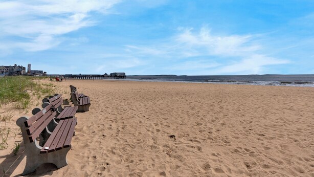 A sandy beach with wooden benches and a pier in the background. - The Inn at SOHO Square (Old Orchard Beach)