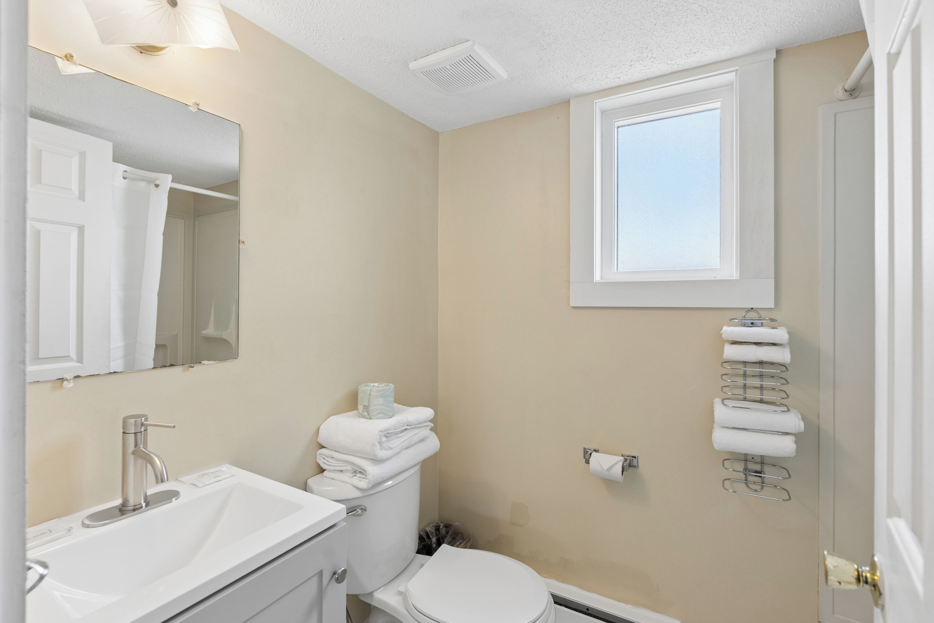 A bathroom with a sink, toilet, mirror, towel rack, and a window.