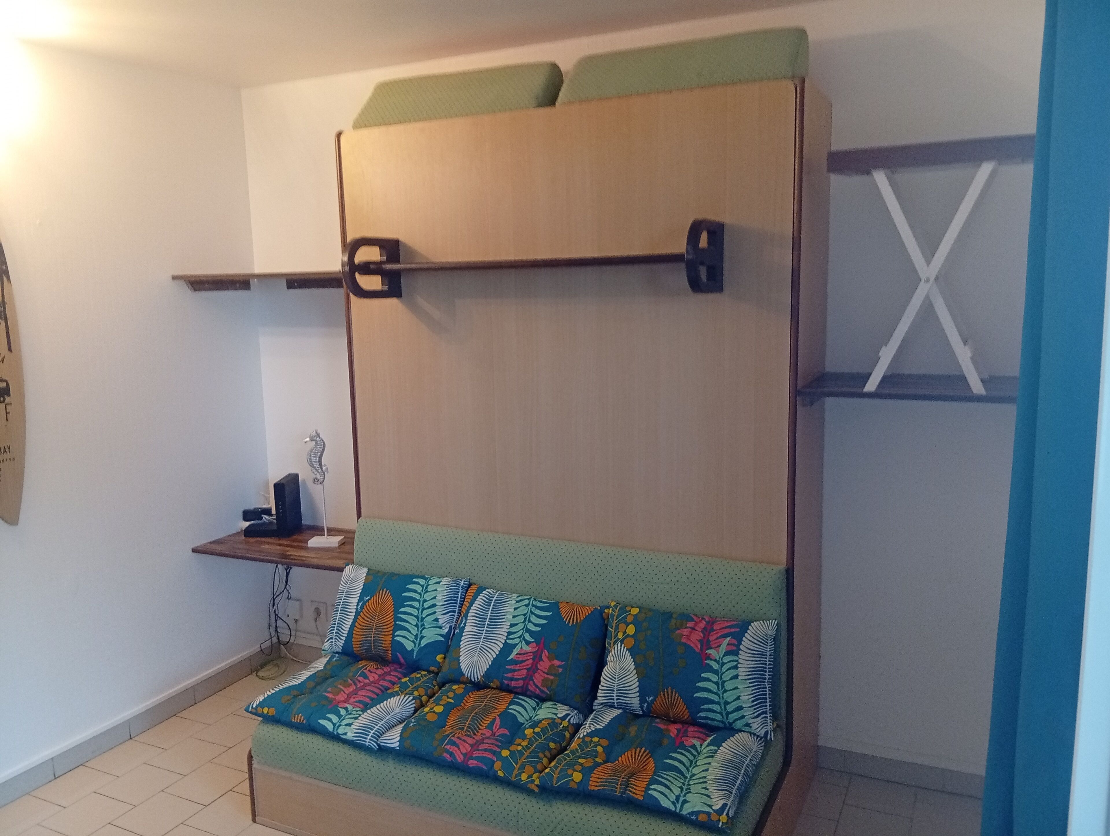 A room with a bunk bed, a sofa with colorful cushions, a small table, and a wall-mounted shelf.