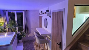 Een kamer met een schuifglasdeur, een klein barretje met krukken, een potplant en een houten trap.
