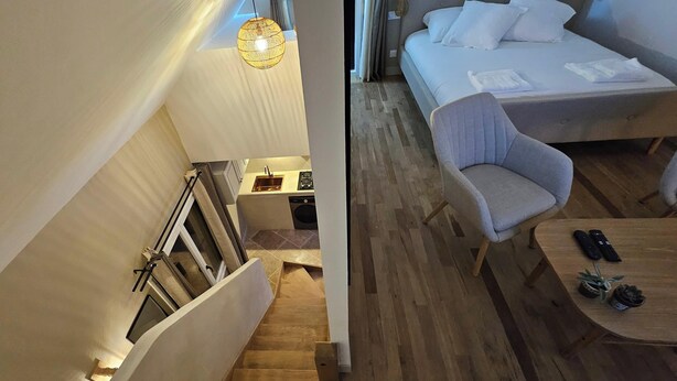 Een moderne hotelkamer met een trap, een bed met witte lakens, een grijze fauteuil en een klein tafeltje met afstandsbedieningen.