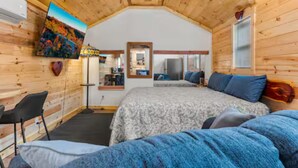 Een slaapkamer in een houten blokhut met een bed, een stoel, een spiegel en een schilderij aan de muur.