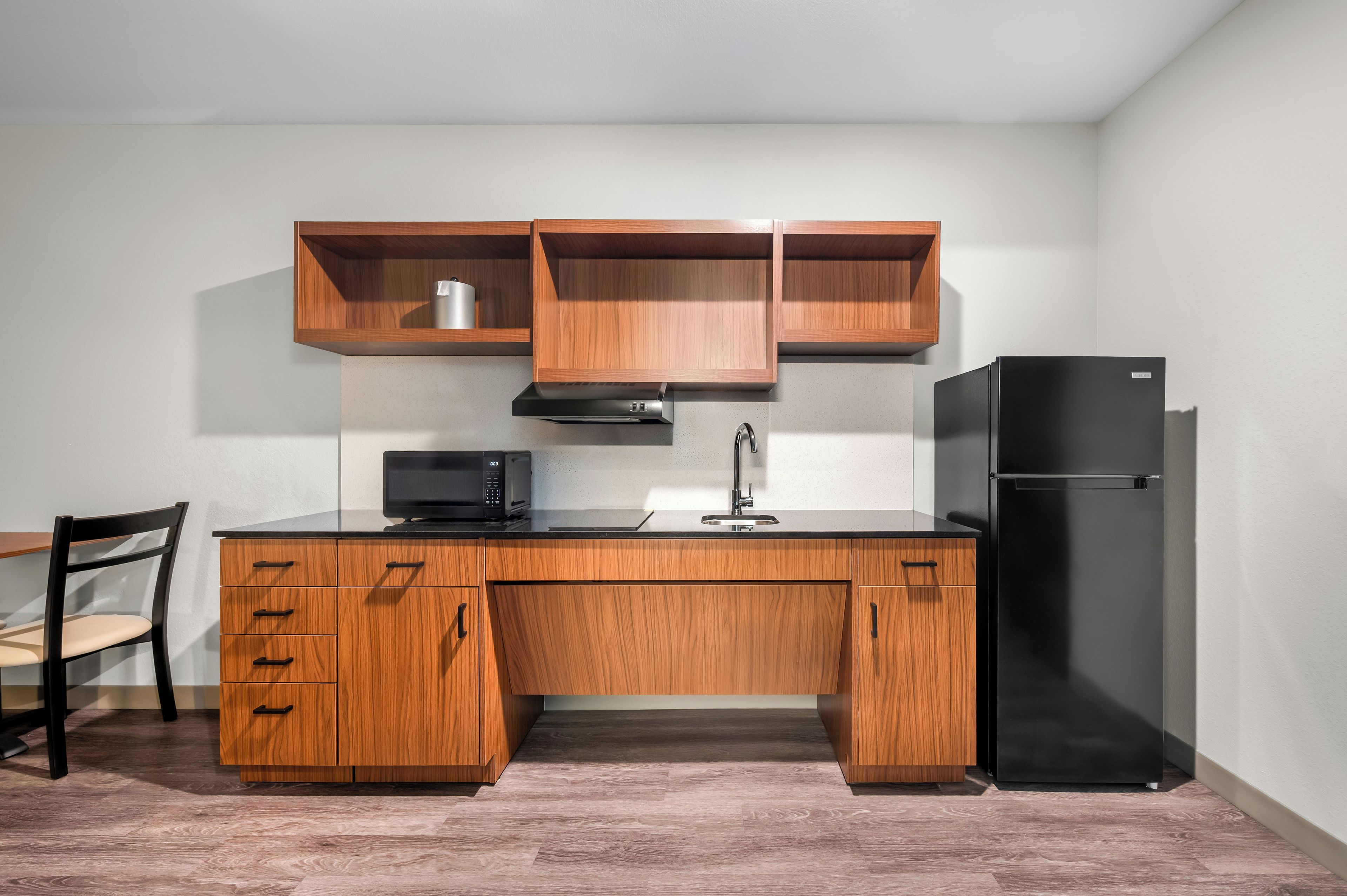 Una cocina con armarios de madera, un refrigerador negro, un microondas y un fregadero.