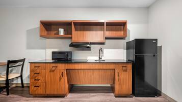 Eine Küche mit Holzausstattung, einem schwarzen Kühlschrank, einer Mikrowelle und einem Spülbecken.