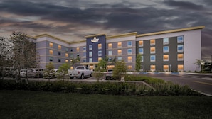 A multi-story hotel with a flat roof, a central entrance, and a parking lot in front. - HomeTowne Studios by Red Roof Fort Myers (Fort Myers)