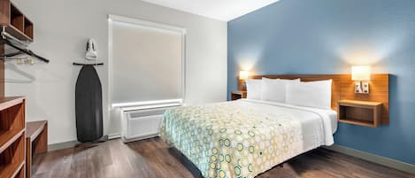 Habitación de hotel con cama, suelo de madera, ventana, calentador, estante con zapatos y lámpara fijada a la pared.