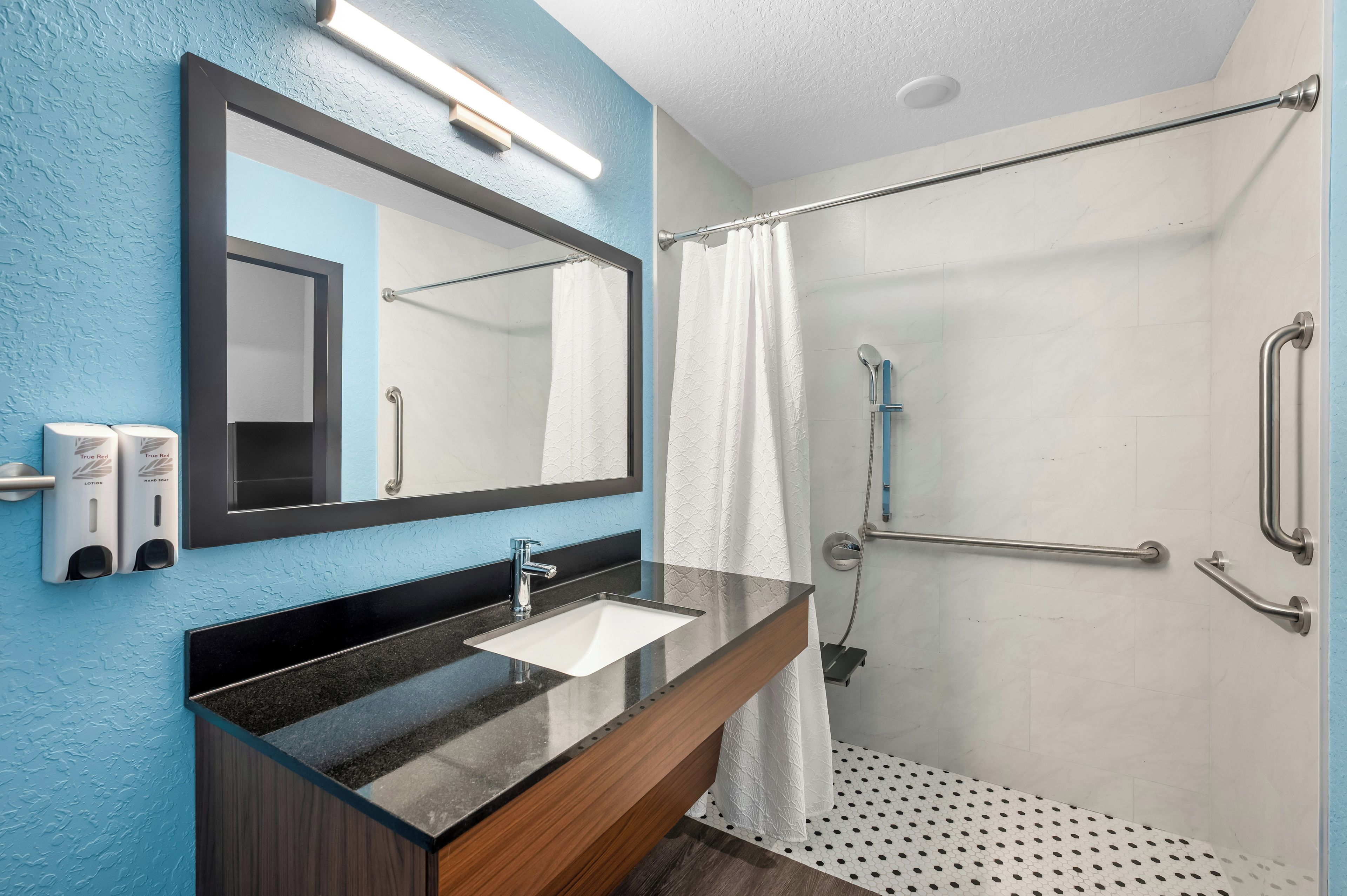 A bathroom with a mirror, sink, and shower.