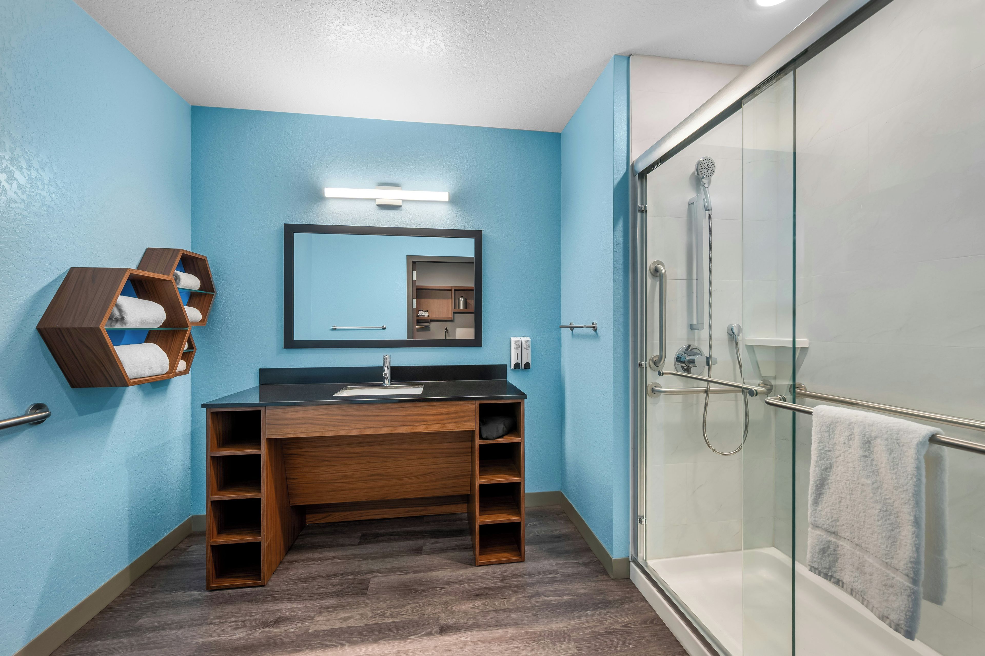 A bathroom with a wooden vanity, a glass shower enclosure, and a blue wall.