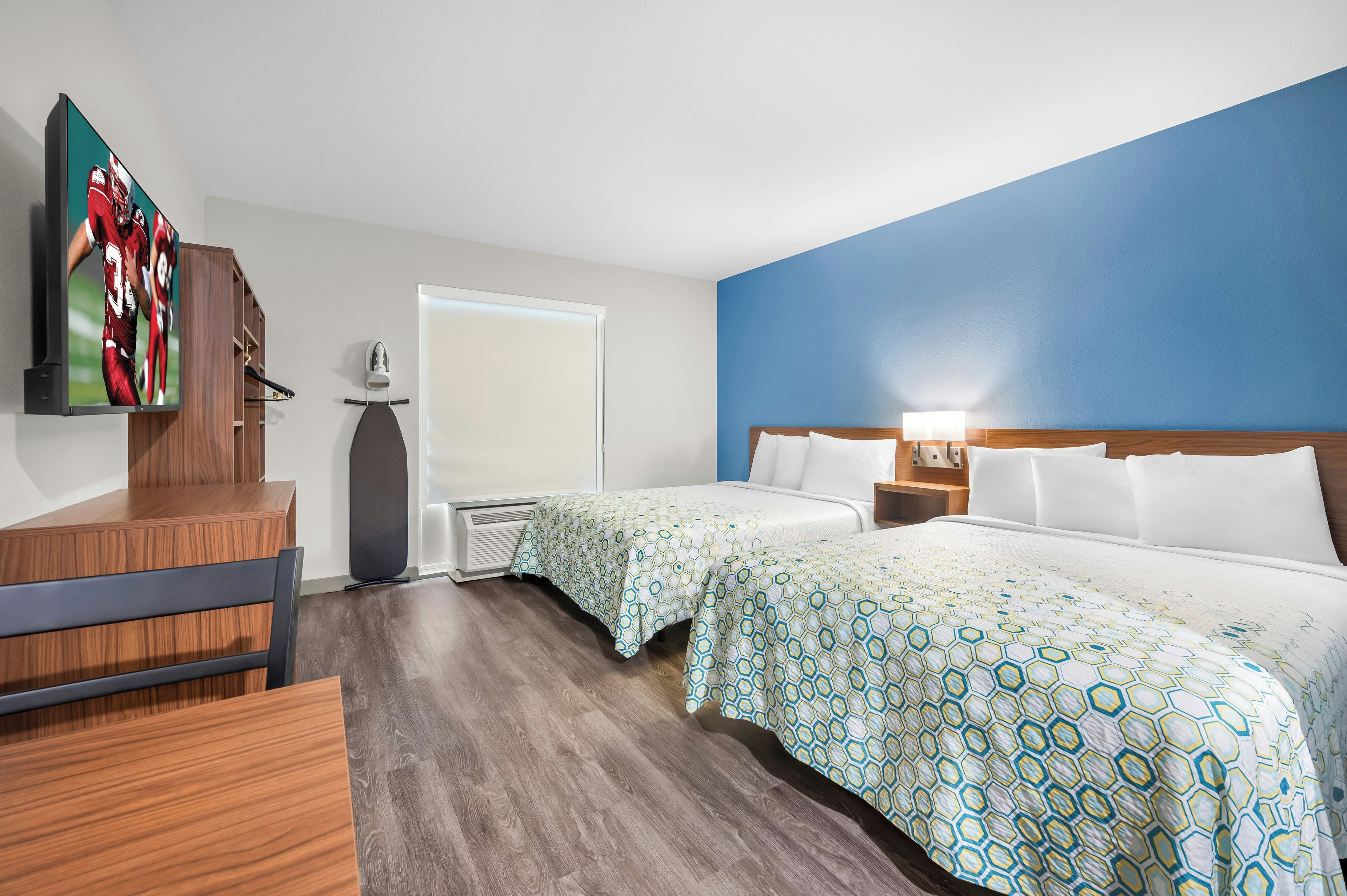 Habitación de hotel con cama, dos mesitas de noche, escritorio, silla, televisor y ventana.